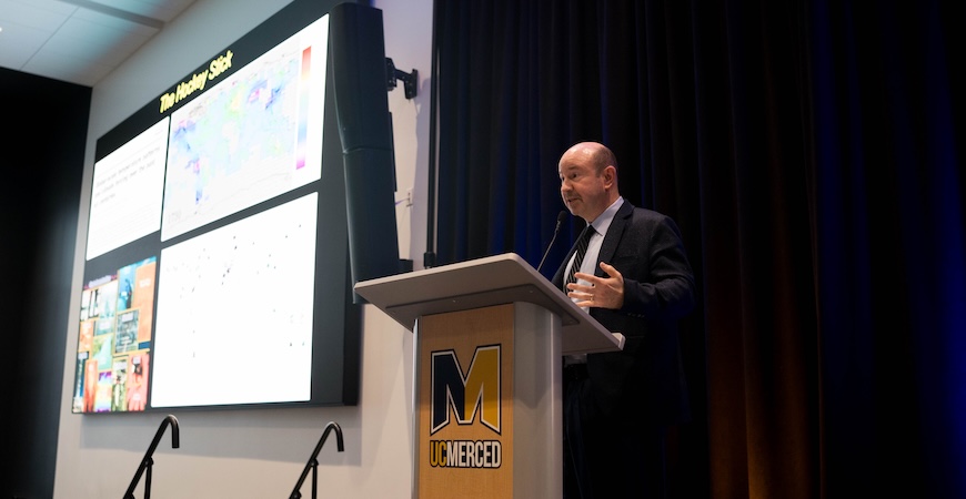 Photo depicts climate scientist Michael Mann speaking at a podium at UC Merced.